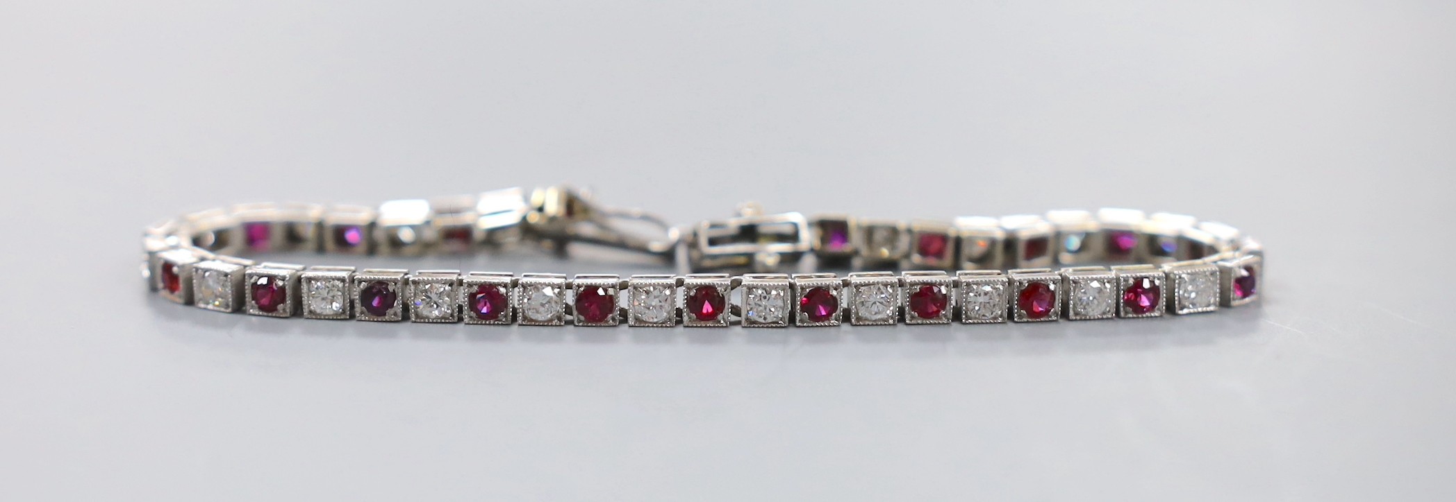 A modern white metal, twenty one stone ruby and twenty three stone diamond set line bracelet, 17.3cm, gross weight 12.5 grams.